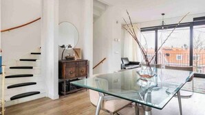 A modern dining area with a glass table, chairs, a wooden cabinet, and a staircase.