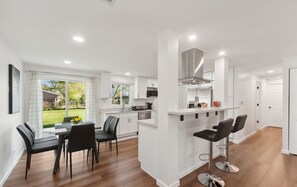 A modern kitchen with white cabinets, a stainless steel range hood, and a dining area with a table and chairs. - Charming 3-bedroom/ 2 Bath Single Family Home/ Schaumburg (Schaumburg)