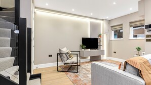 Una sala de estar moderna con una escalera, un televisor de pantalla plana, un sofá y una mesa de centro.