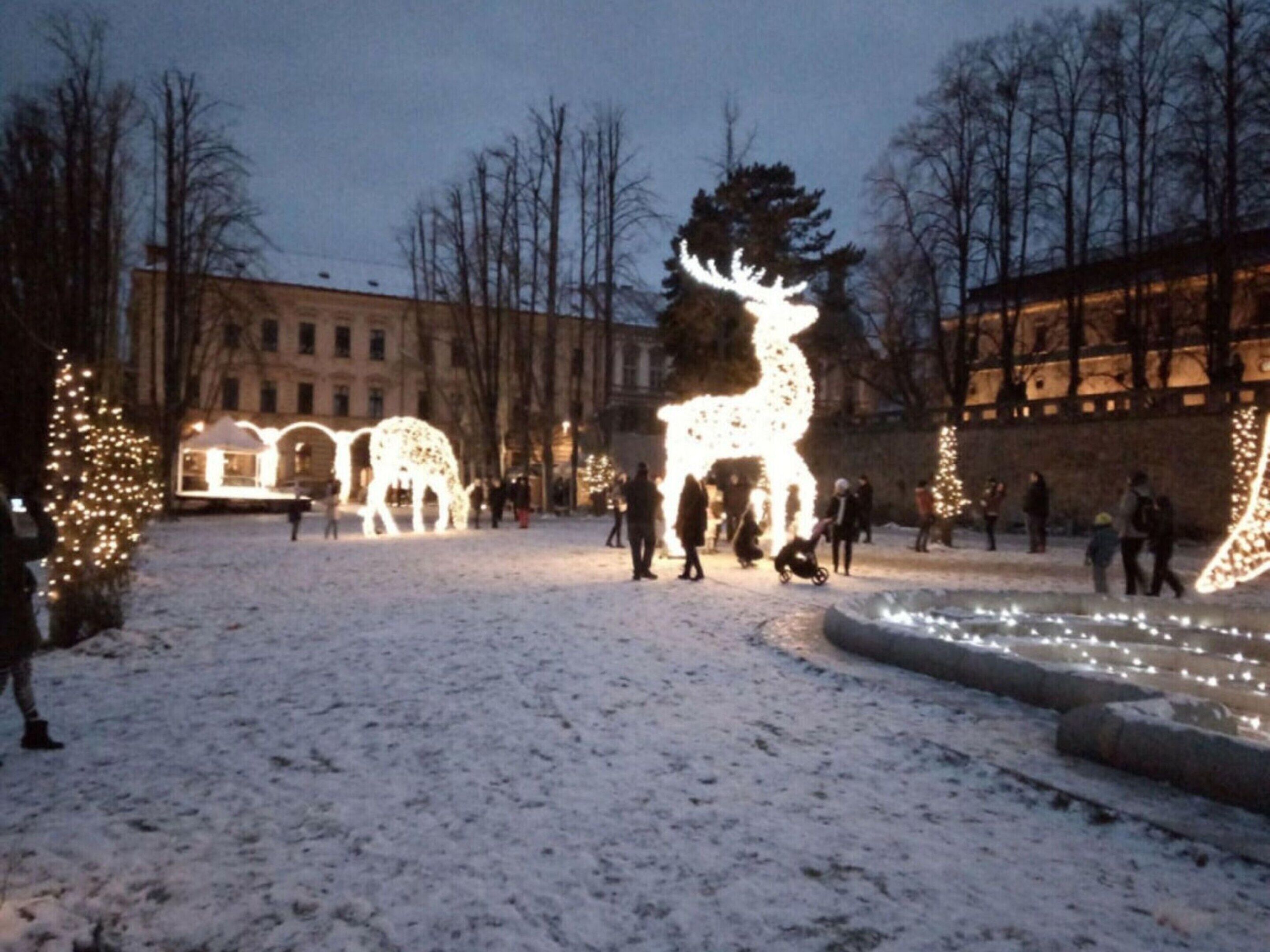 Un patio cubierto de nieve con esculturas iluminadas de renos y un edificio al fondo.