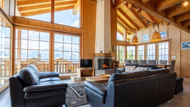 A spacious living room with a fireplace, large windows, and a view of the mountains.