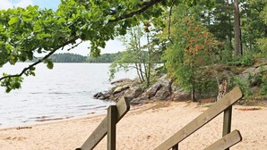 A wooden bench overlooking a sandy beach with a lake and trees in the background. - 4 Star Holiday Home in Kalv (Kalv)