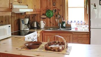 Una cocina con armarios de madera, estufa, pileta y diversos utensilios de cocina.