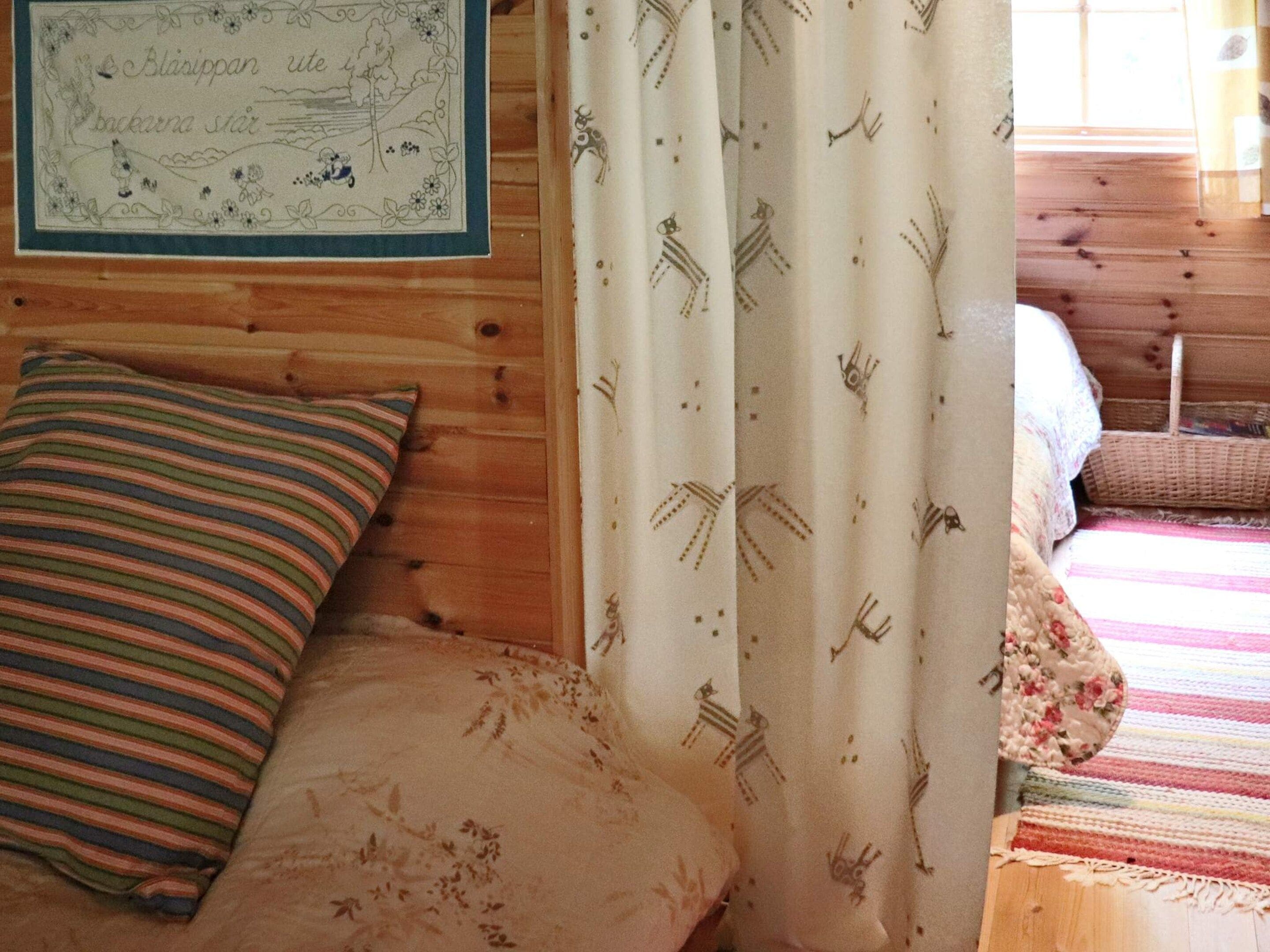 A wooden cabin interior with a bed, striped pillow, and a curtain with animal prints.