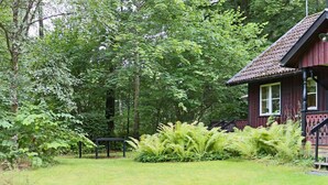 A rustic wooden cabin with a red roof, surrounded by lush greenery and ferns. - 4 Star Holiday Home in Kalv (Kalv)
