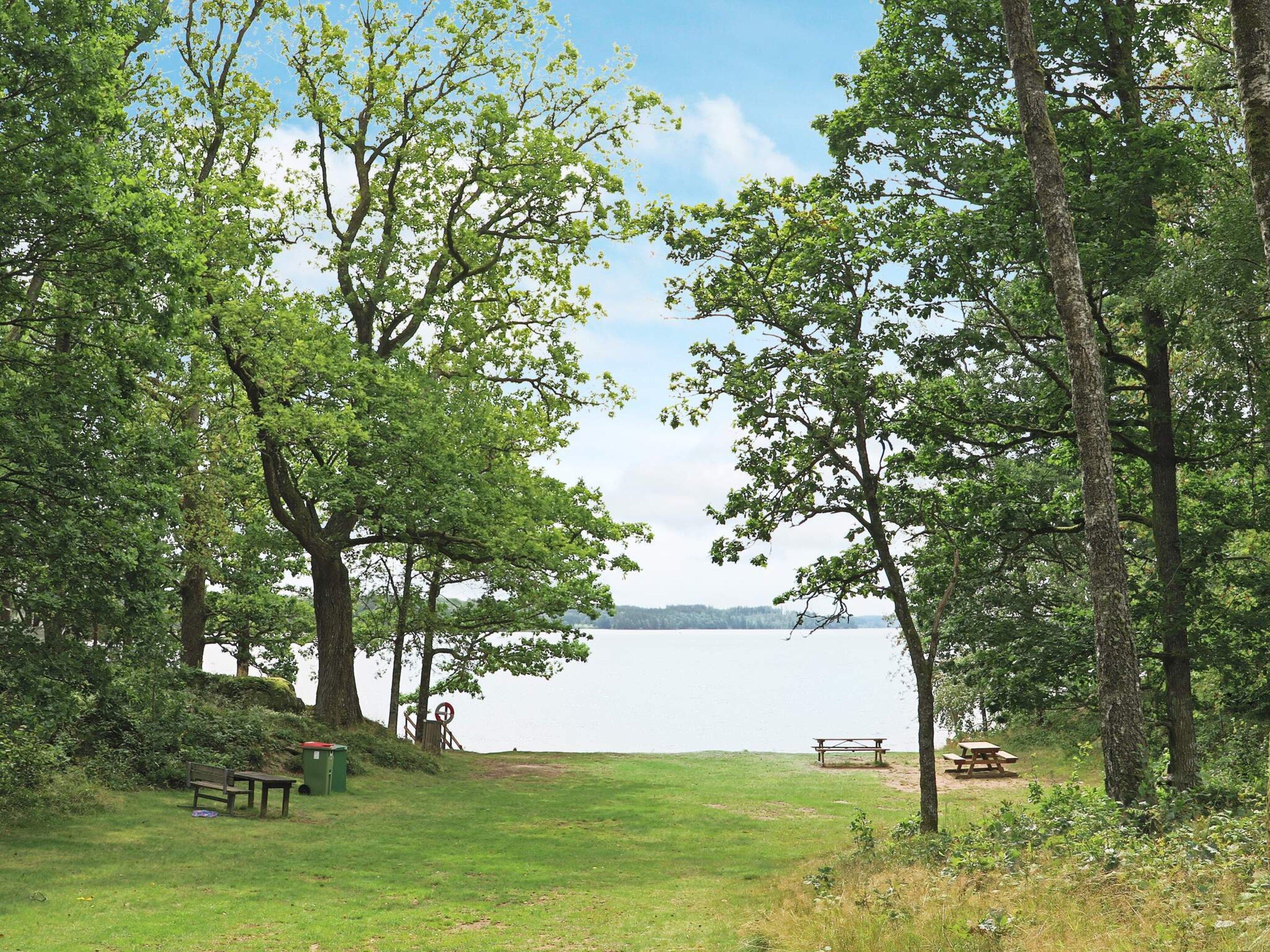 A park with picnic tables and benches, a grassy area, and a lake in the background.