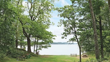 A park with picnic tables and benches, a grassy area, and a lake in the background.