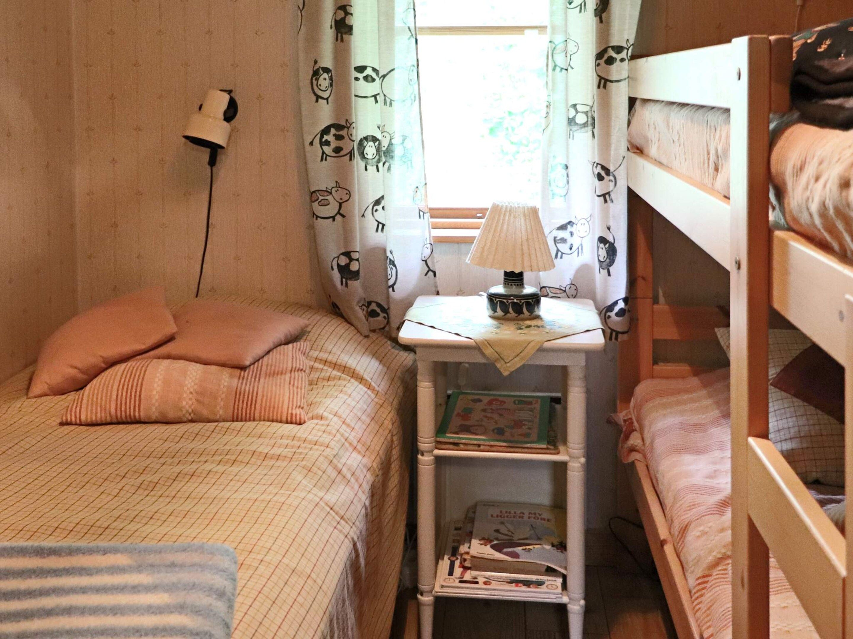 Une chambre avec un lit superposé, une table de chevet, une lampe et une fenêtre avec des rideaux.