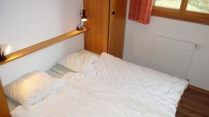 Ein Einzelbett in einem Zimmer mit Holzboden und einem Vorhangfenster.