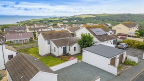 A residential area with houses, some with solar panels, and a view of the sea and hills in the background. - PuffinPatch - Beachside Cottage (Broad Haven)