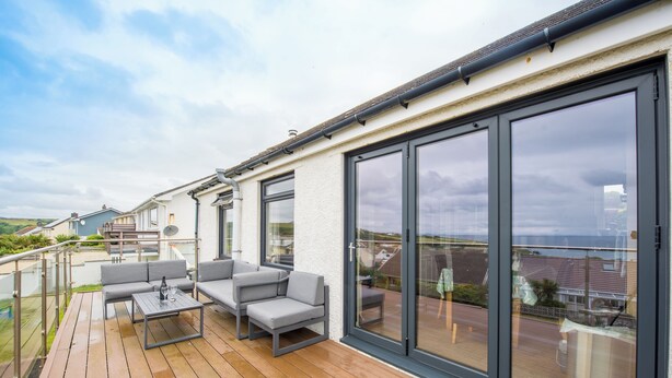 A deck with outdoor furniture and large sliding glass doors. - PuffinPatch - Beachside Cottage (Broad Haven)