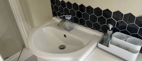 A bathroom with a white sink, a black hexagonal tile backsplash, and a cup holder with a bottle.