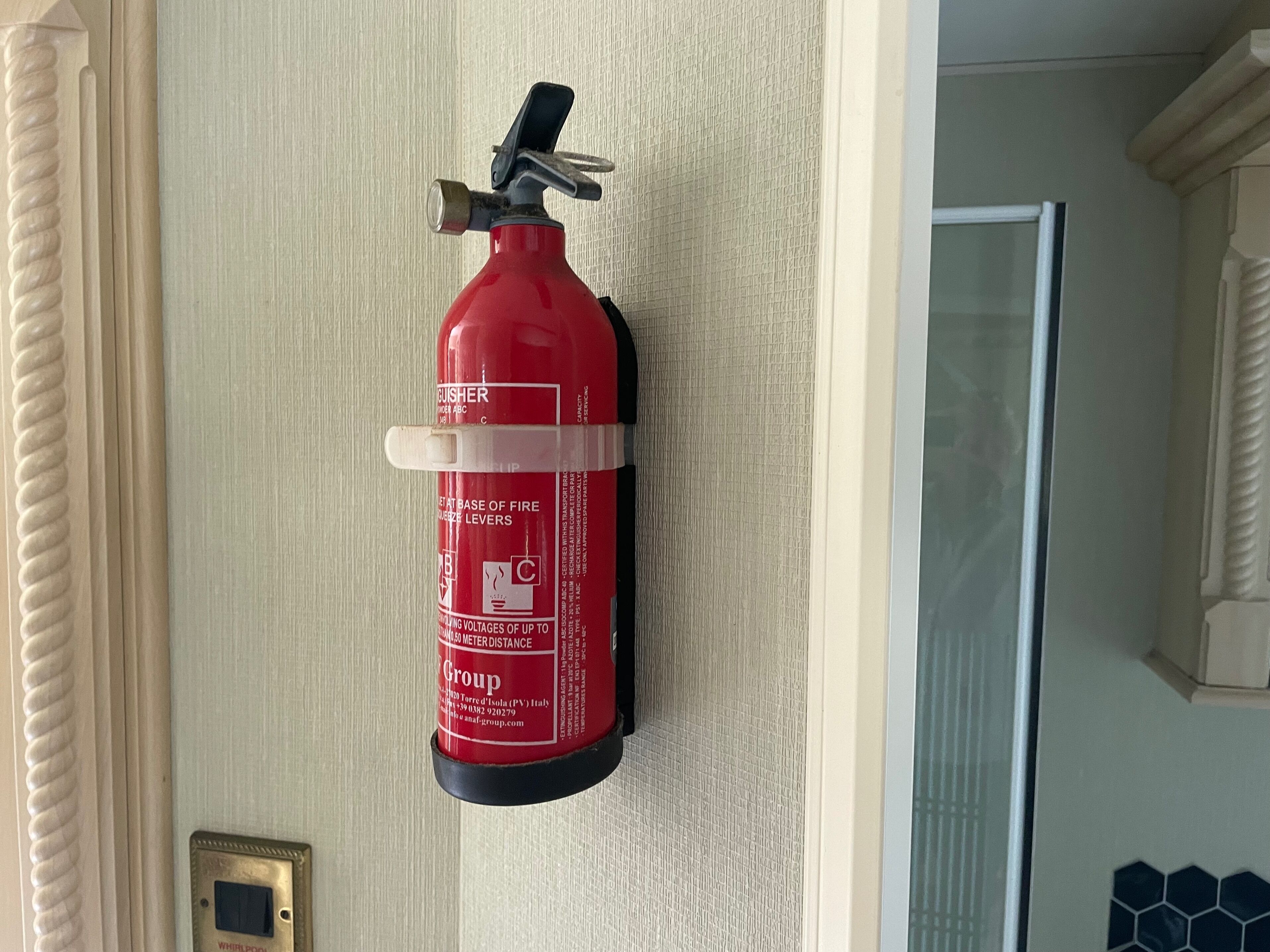 Un extintor rojo montado en una pared con textura cerca de una puerta.