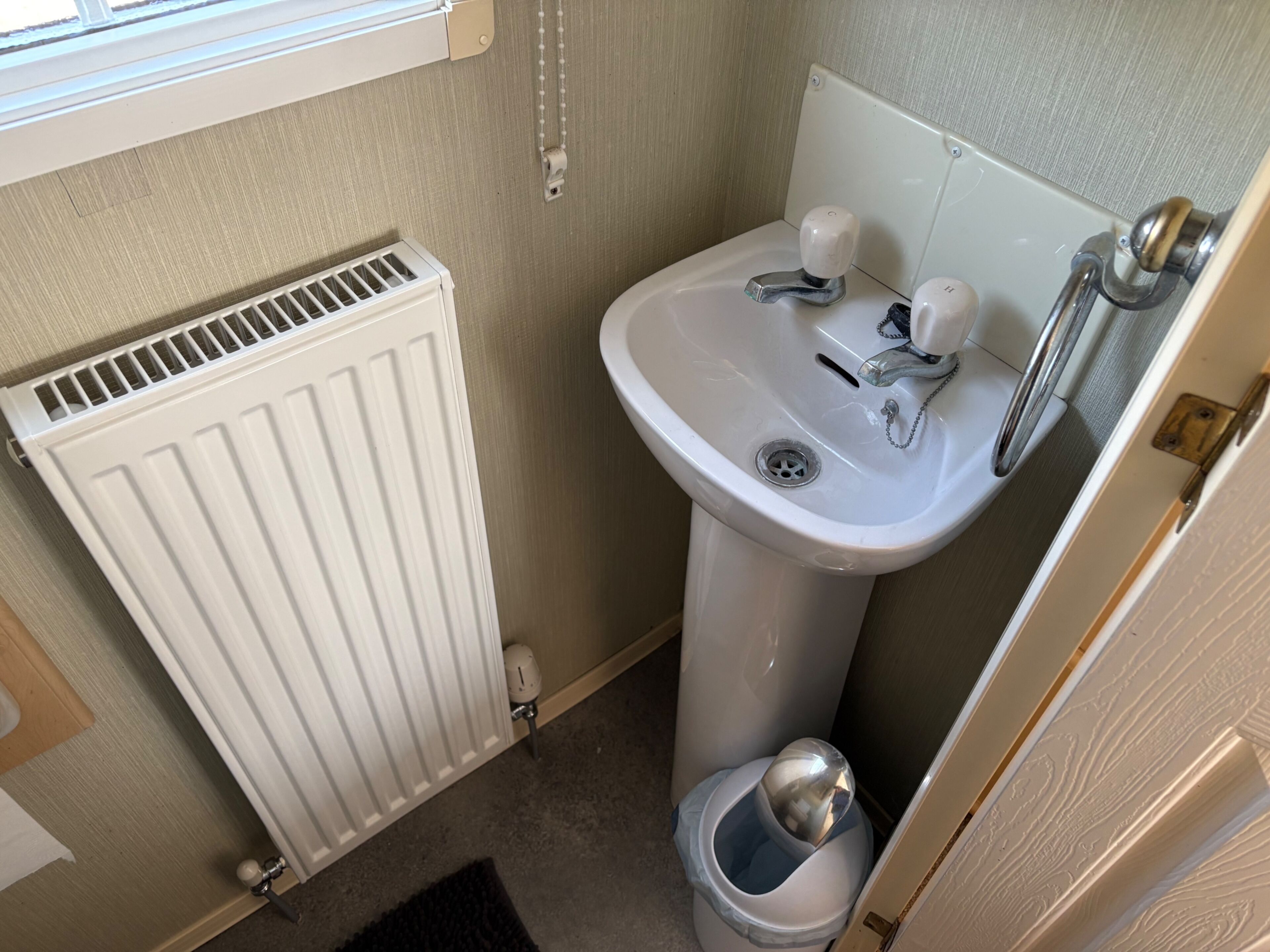 A compact bathroom with a white radiator, a sink with a single faucet, and a trash bin.