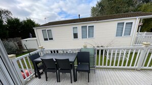 A deck with a table and chairs, a white railing, and a house in the background. - 2 Bed Lodge Sleeps 5 - Pet Friendly, Wifi, Parking (Skegness)