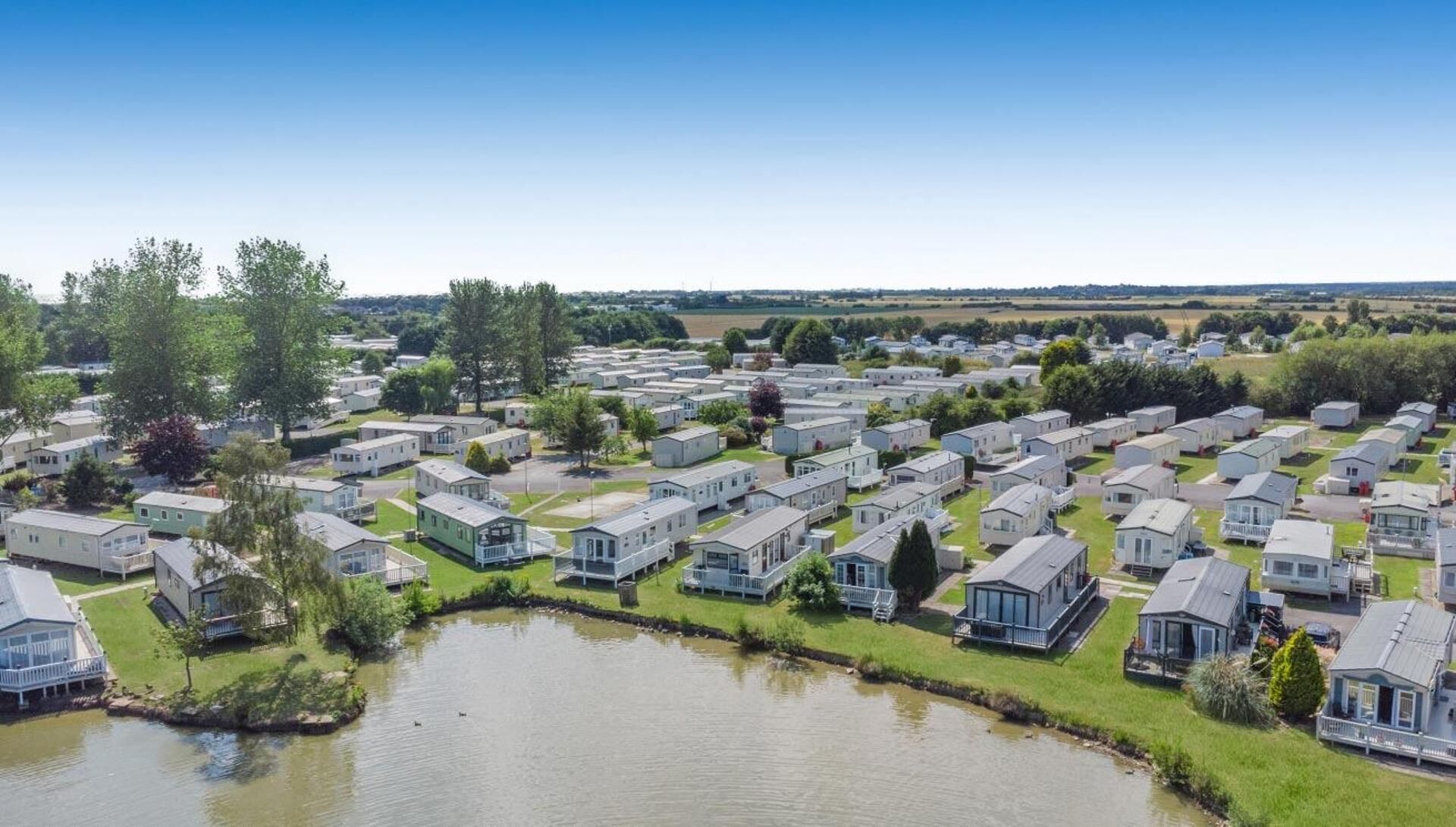 Ein großer Caravanpark mit mehreren Stellplätzen, einem kleinen See und umgebender Bepflanzung.