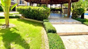 A covered outdoor area with a tiled roof, surrounded by well-maintained greenery and a pool. - Carey Apartment in Carey Residential, White Sands, 5 Minutes from the Beach. (Punta Cana)