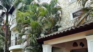 A building with a white facade, a red-tiled roof, and a covered entrance with white columns. - Carey Apartment in Carey Residential, White Sands, 5 Minutes from the Beach. (Punta Cana)