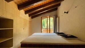 A bedroom with a wooden ceiling, a bed with a mattress and pillows, and a window with a view of greenery.