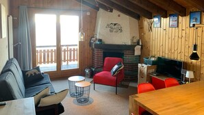 A cozy room with a fireplace, wooden walls, a sofa, a red chair, and a dining table.