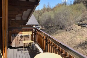Une terrasse en bois avec une table et des chaises, offrant une vue sur un paysage vallonné.