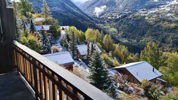 Un chalet de montagne doté d’une terrasse en bois offrant une vue sur une vallée où les arbres et les montagnes sont recouverts de neige.