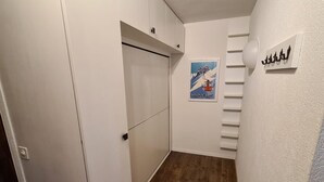 Un couloir étroit aux murs blancs, avec un plancher en bois et une porte donnant sur un placard. Une affiche du Mont Blanc est accrochée au mur, et une petite étagère est visible.