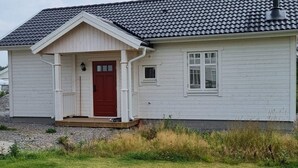 Une maison de plain-pied avec une porte rouge, un revêtement extérieur blanc et un toit recouvert de tuiles grises.