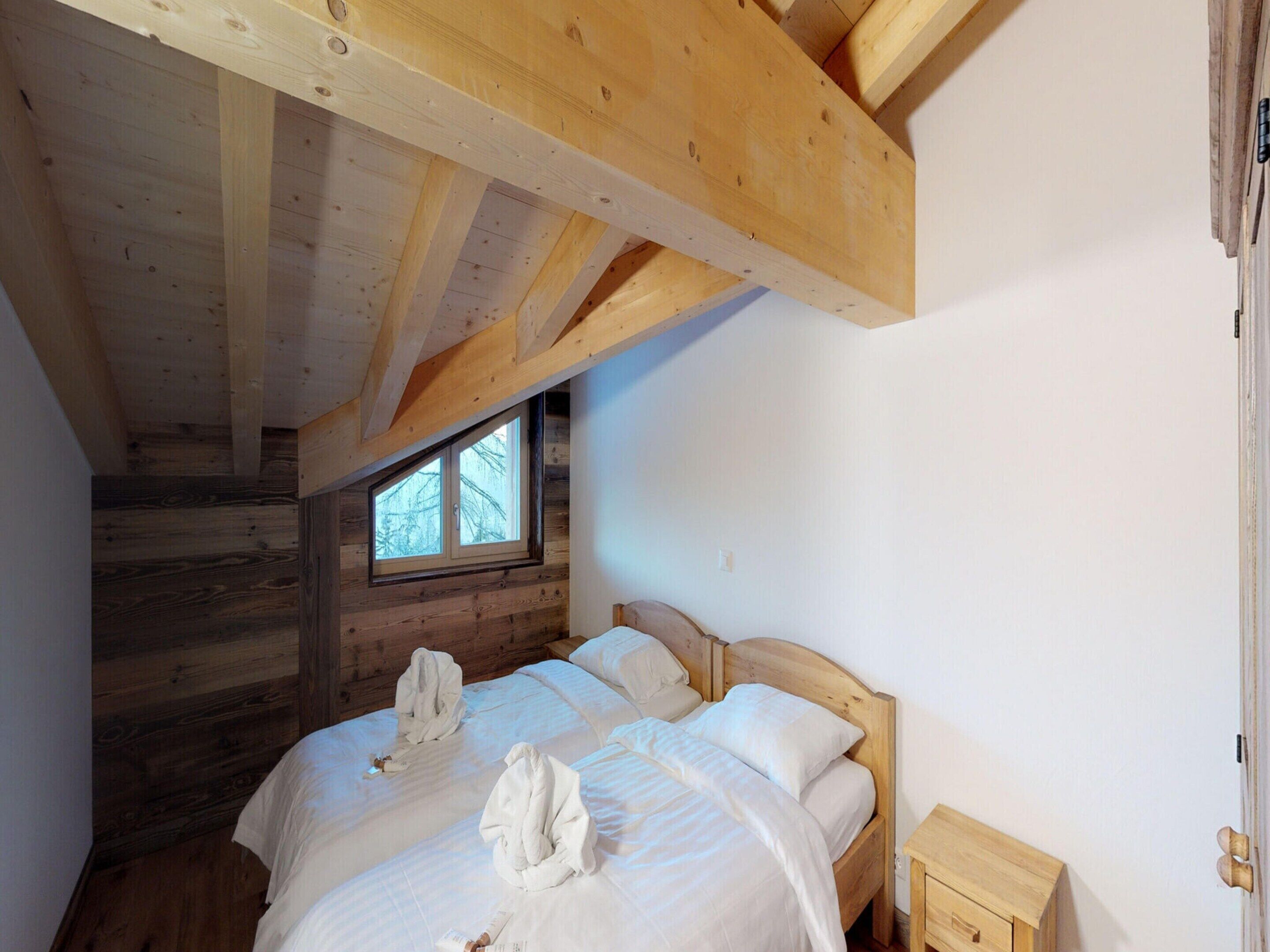 Une chambre avec deux lits, des poutres en bois, une fenêtre et une table de chevet en bois.