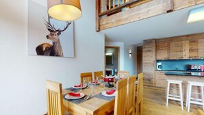 A dining area with a wooden table set for six, surrounded by chairs. A large painting of a deer hangs on the wall. The room has wooden flooring and a loft area with a wooden railing. - Spacious Apartment for ski Holiday (Veysonnaz)