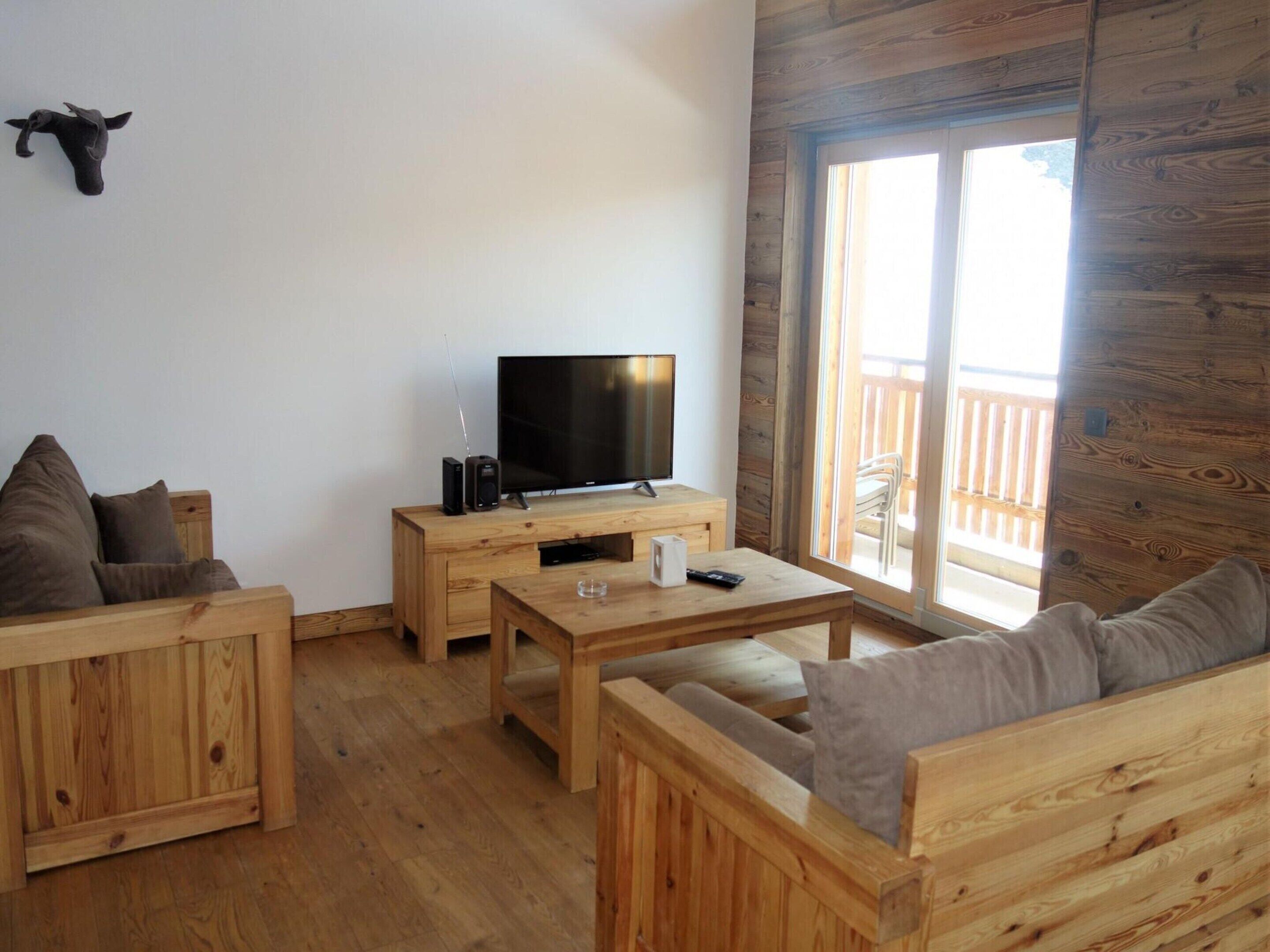 A wooden interior with a TV on a wooden stand, a sofa, and a table.