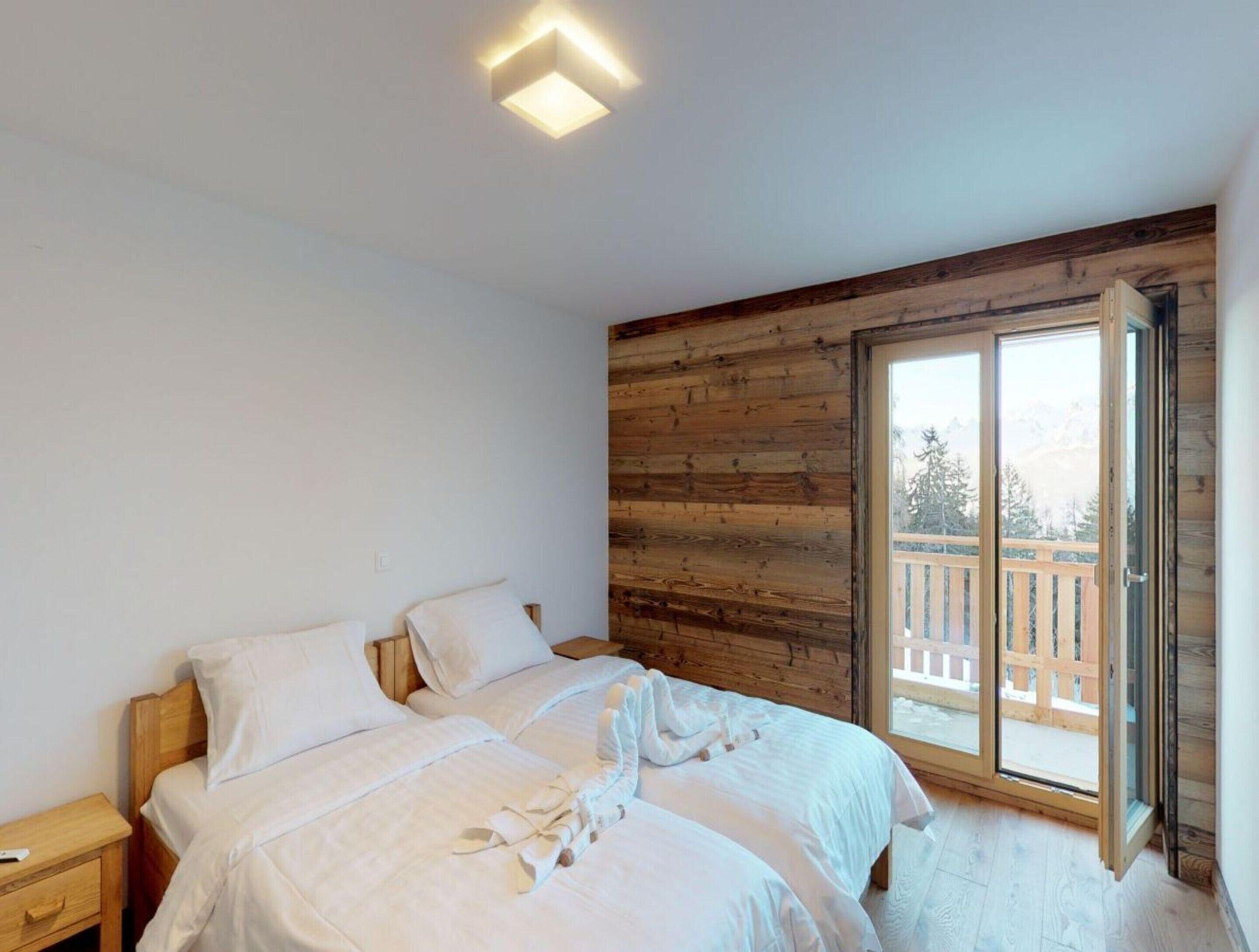 Une chambre avec deux lits, un mur recouvert de lambris en bois et une grande porte-fenêtre coulissante donnant sur un balcon extérieur.