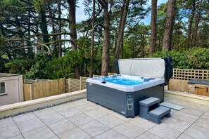 Un bain à remous sur une terrasse carrelée, avec une clôture en bois et des arbres en arrière-plan.