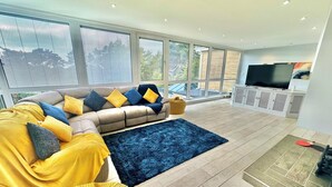 Una sala moderna con un sofá modular, una alfombra azul y un televisor sobre un mueble blanco.