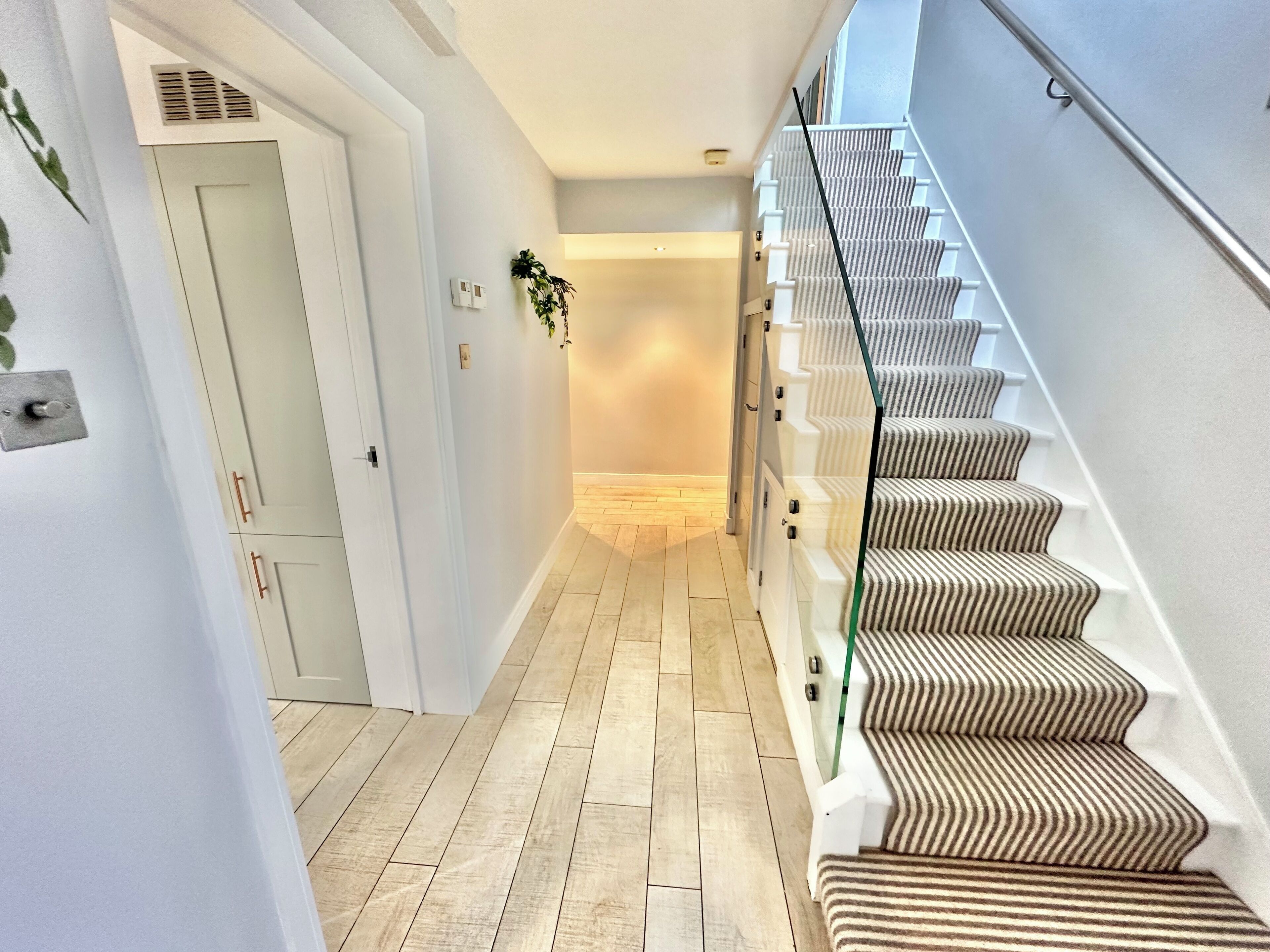 Ein modernes Interieur mit Holzboden, einer mit Streifenmuster versehenen Treppe und einer Tür mit einer Pflanze an der Wand.