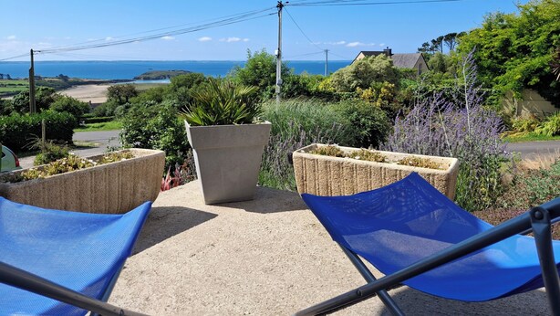 Terraço com duas cadeiras de tela azul, um vaso de concreto e vista para o mar e colinas.