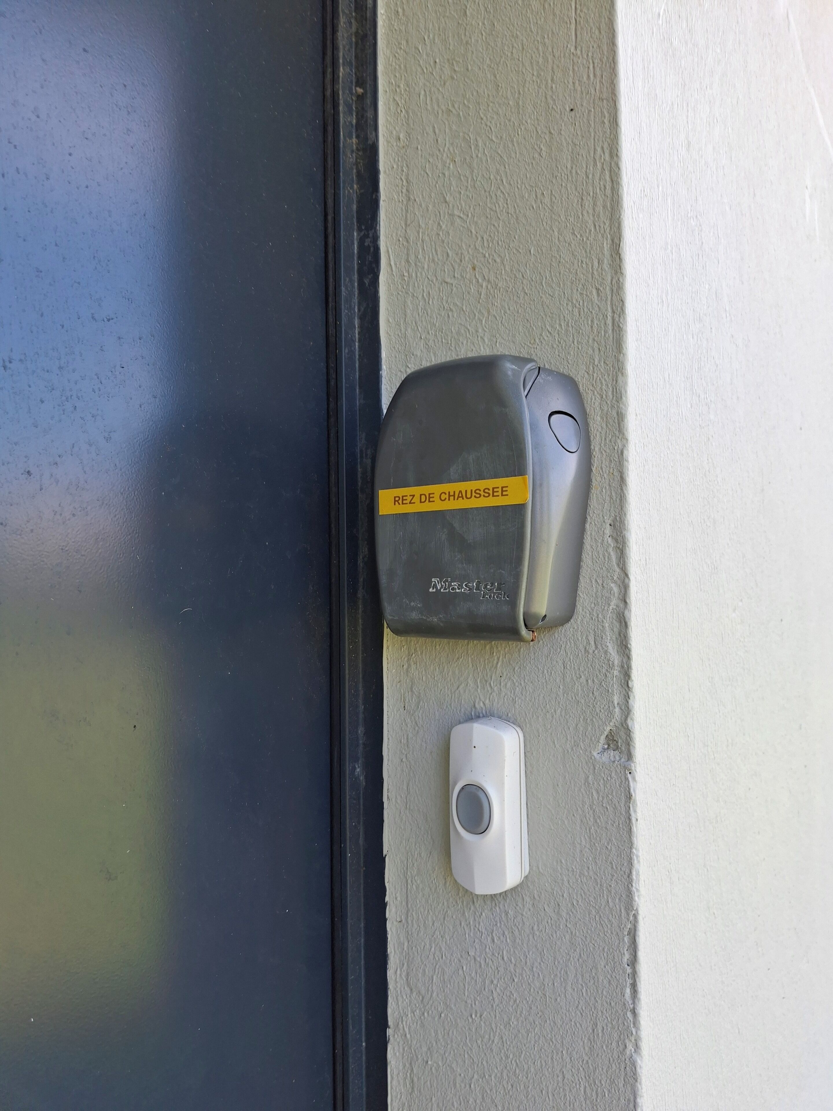 Une porte avec une poignée de porte grise et un petit appareil blanc placé en dessous.
