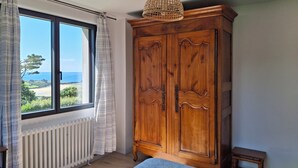 Quarto com uma grande janela, guarda-roupa de madeira e vista para o mar.