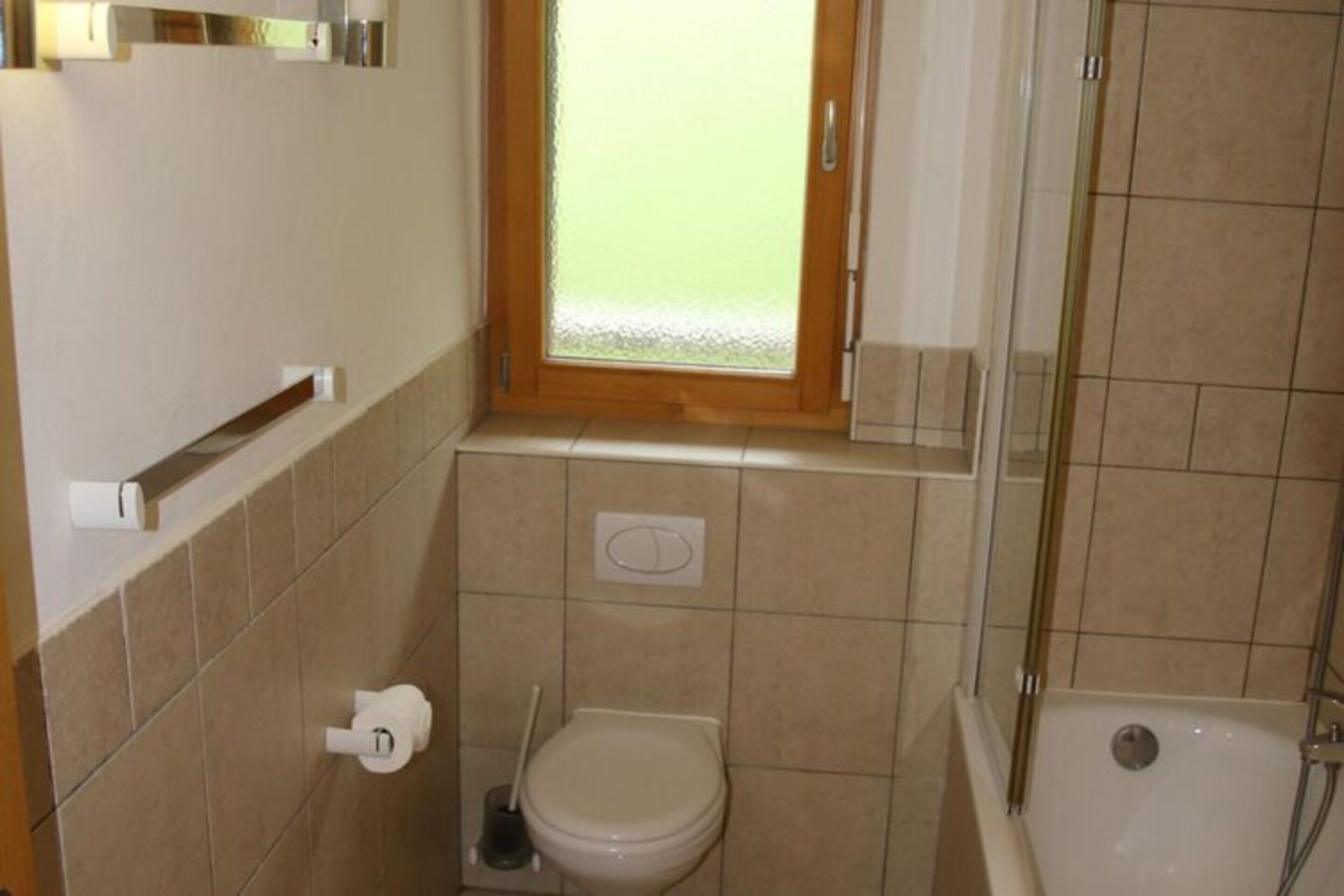 A small bathroom with a toilet, a bidet, a shower, and a window.