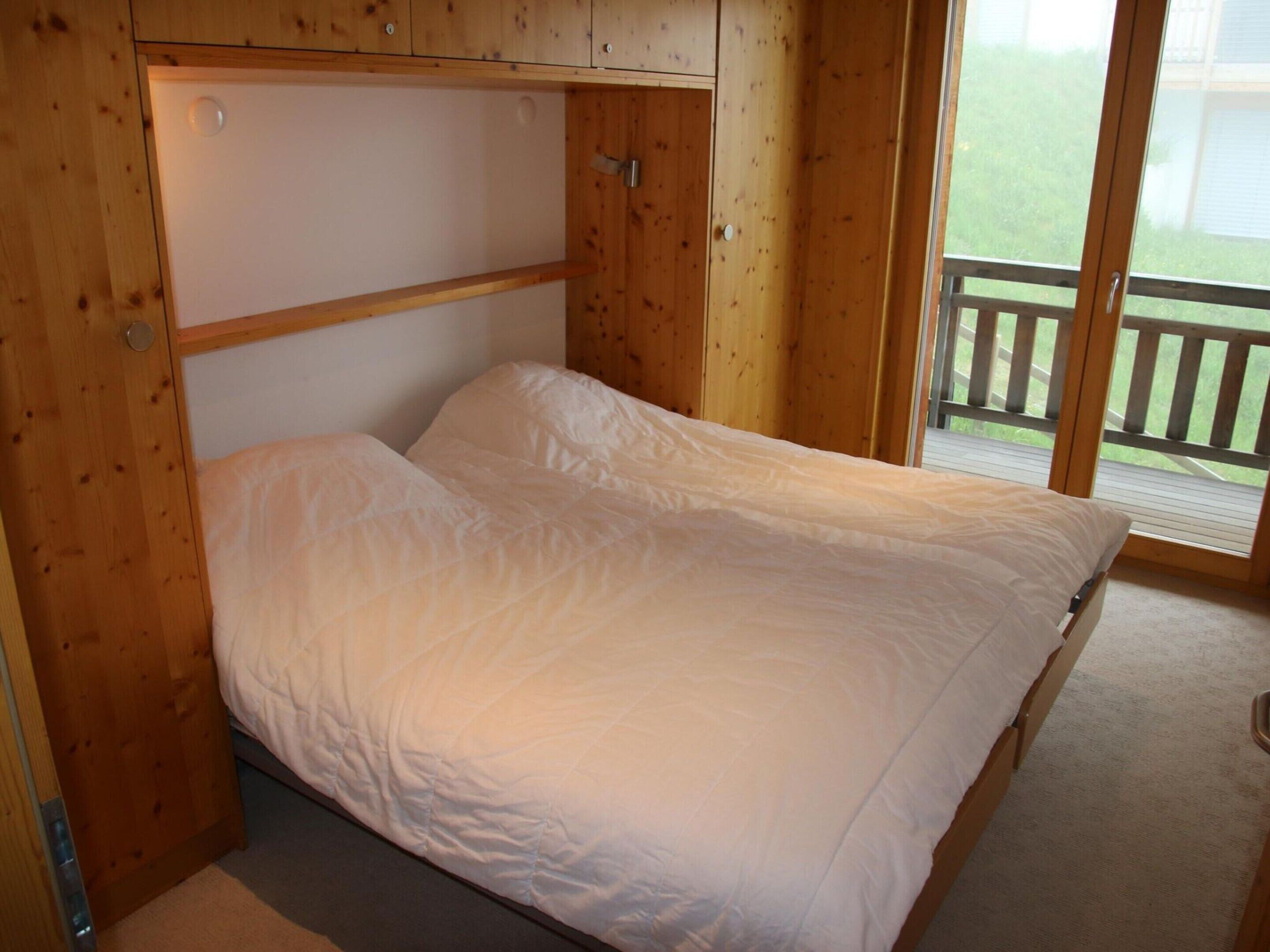 A single bed with a wooden headboard and a view of a balcony.