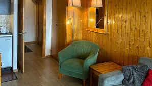 Moderni olohuone, jossa on vihreä nojatuoli, harmaa sohva ja puulattia. Seinässä on puupanelointi ja seinävalaisin.