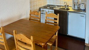 Pieni ja käytännöllinen keittiö, jossa on liesi, pesuallas ja jääkaappi. Keittiön yhteydessä on puinen pöytä, jonka ympärillä on tuoleja, ja seinällä on taulu.