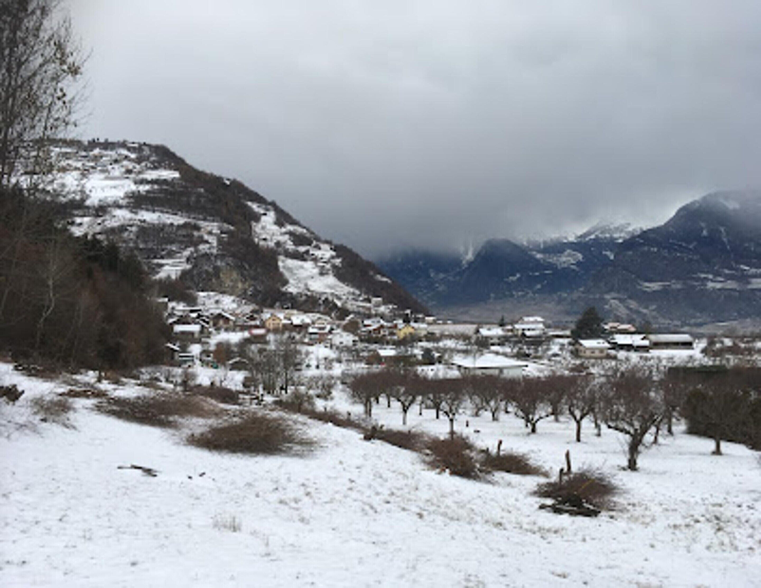 A snow-covered landscape with a village nestled in the valley, surrounded by mountains.