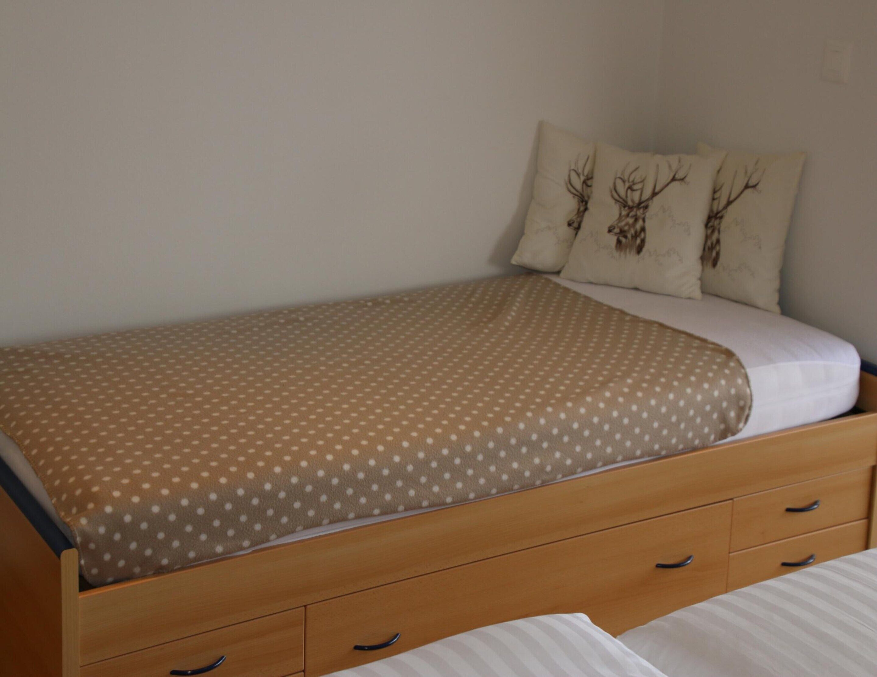 A single bed with a polka dot cover, wooden headboard, and two matching pillows with deer antlers.