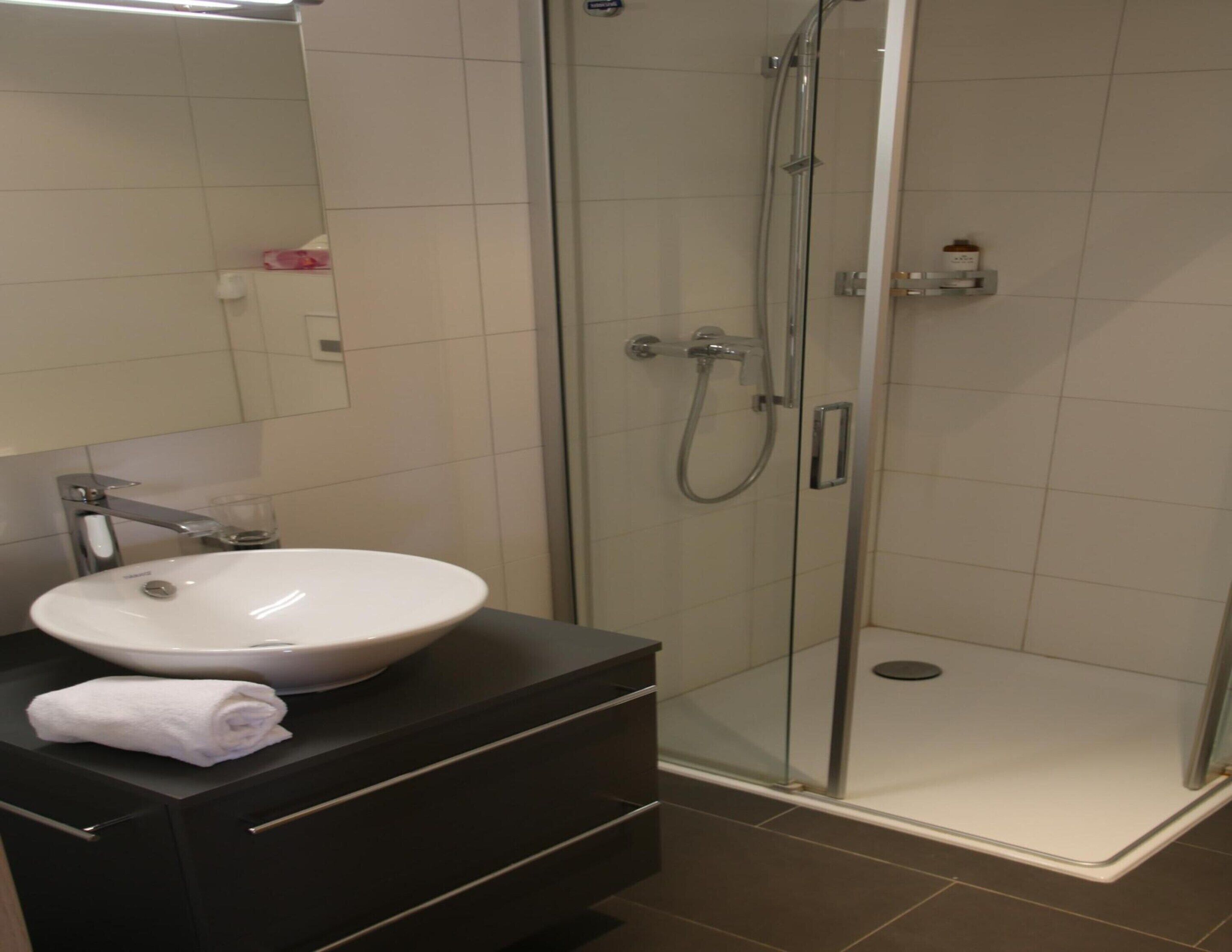 A bathroom with a white sink, a glass shower enclosure, and a dark vanity.