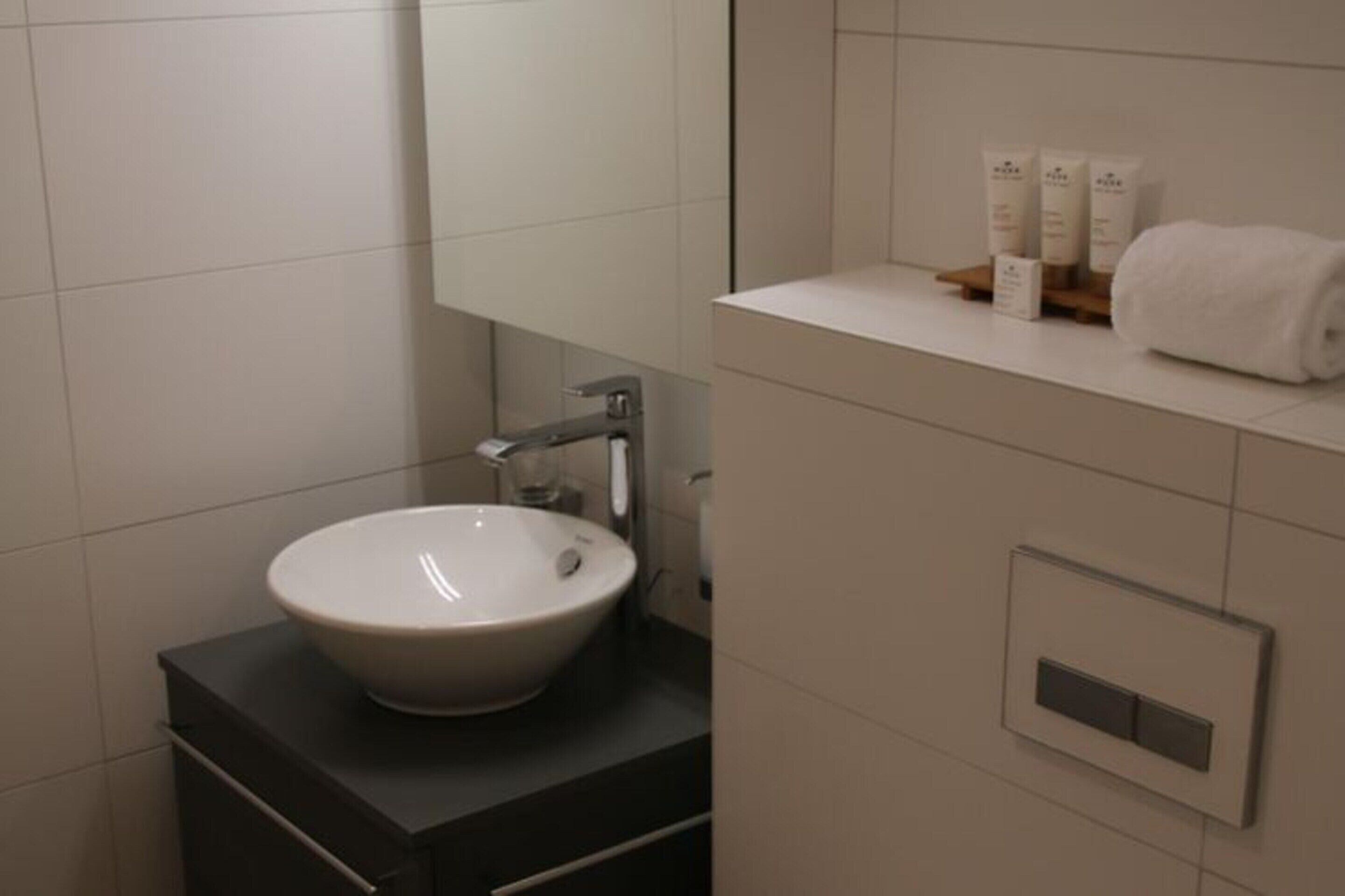 Une salle de bain moderne avec un lavabo blanc, un miroir et une étagère contenant des articles de toilette.