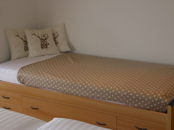 Una cama individual con una colcha de lunares, dos almohadas con diseños de ciervo y un cabecero de madera con cajones.