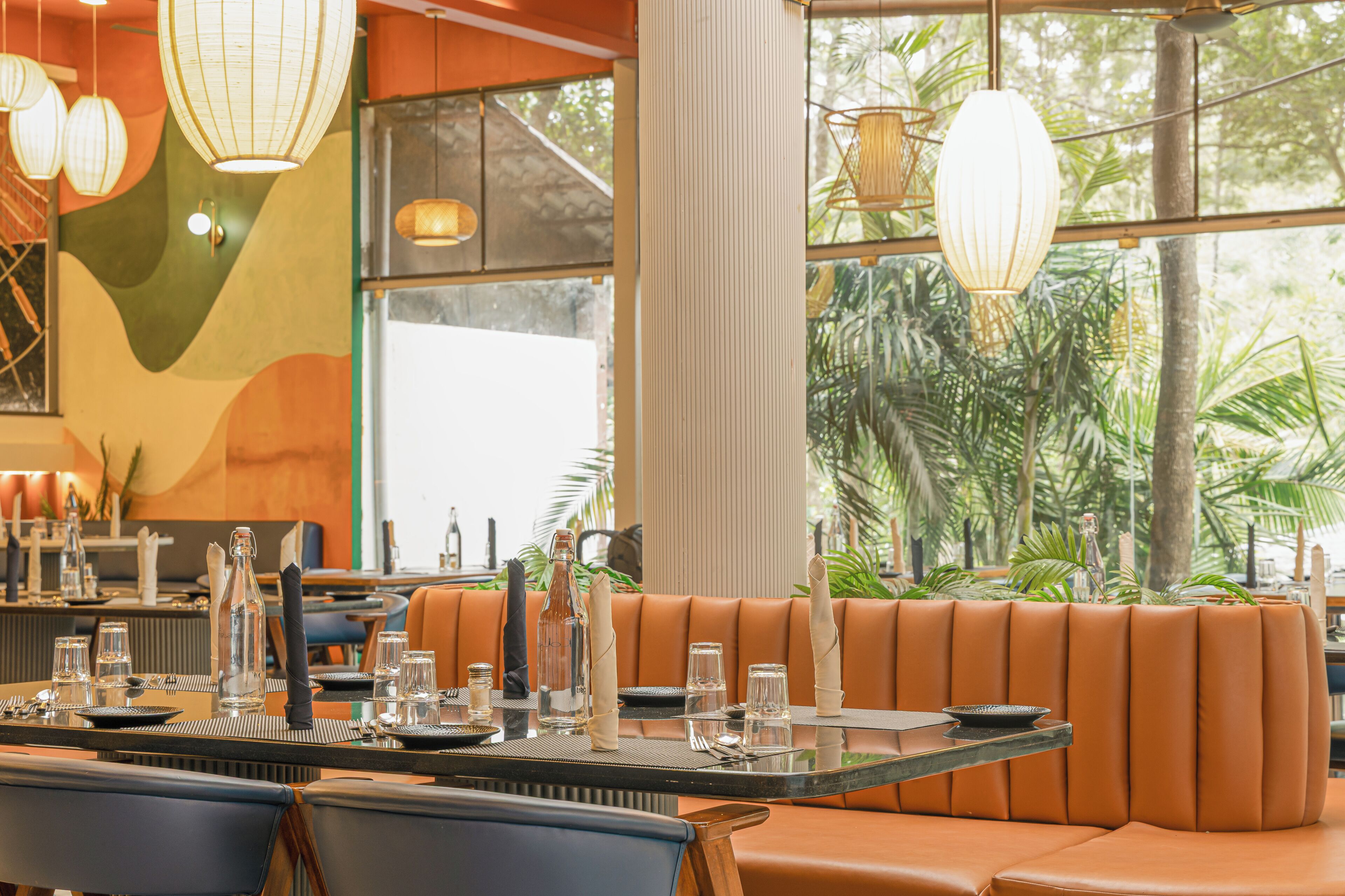 Un restaurant doté d’une longue table dressée pour le dîner, de sièges confortables et de grandes fenêtres offrant une vue sur la verdure.
