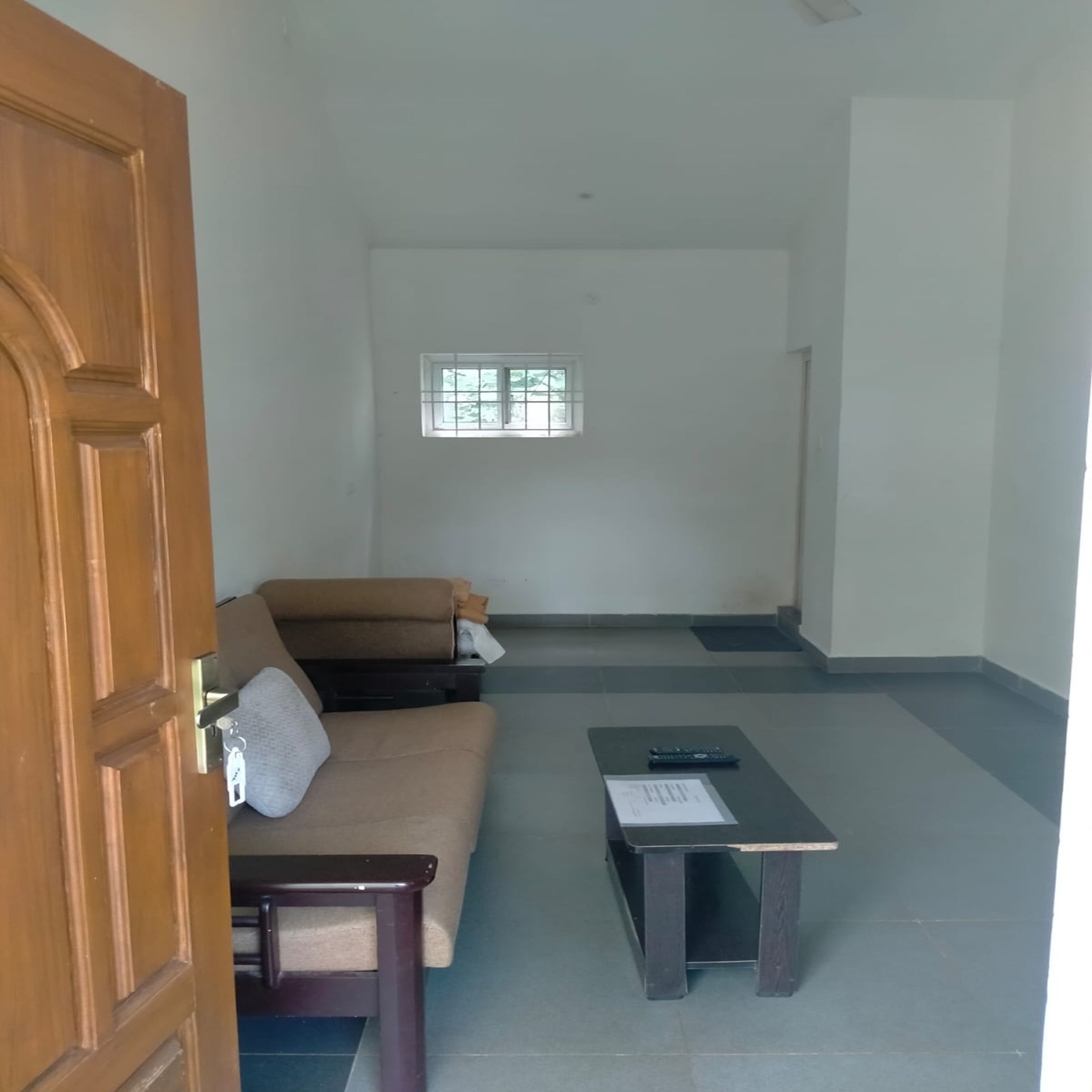 A room with a wooden door, a sofa, a small table, and a window.