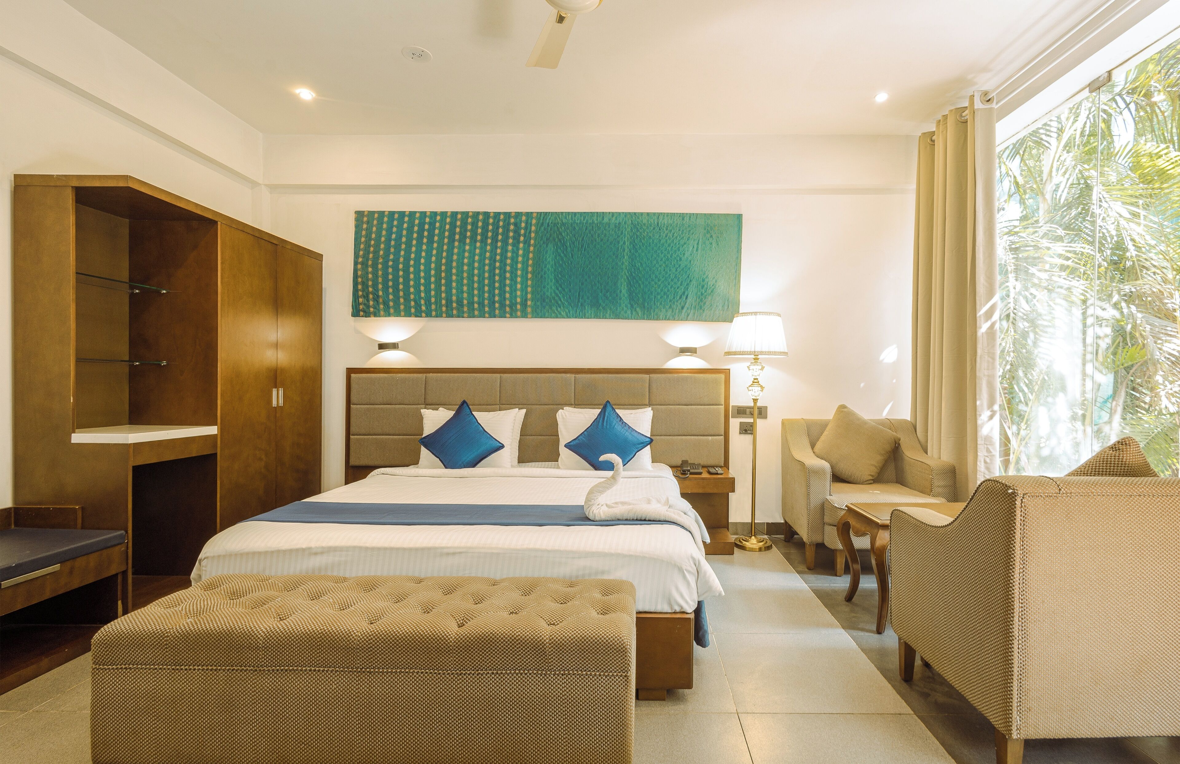 A hotel room with a bed, a desk, a chair, a sofa, and a large window.